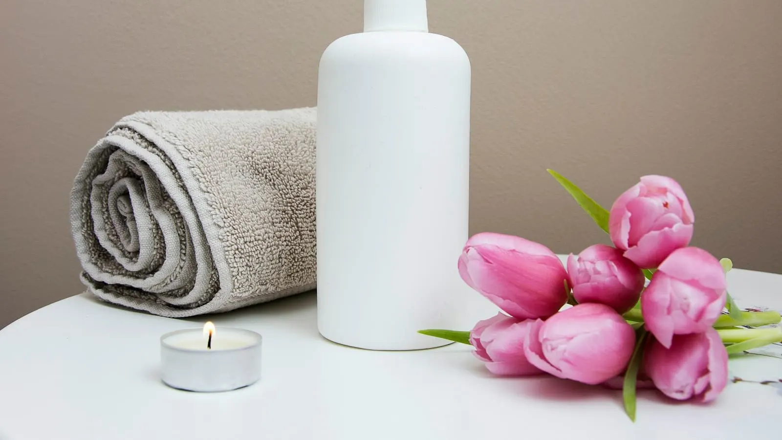 Ambiance spa avec serviette pliée, flacon de soin et tulipes roses